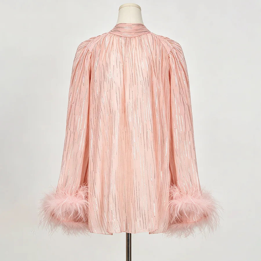 A light pink pleated long-sleeve blouse with feather-trimmed cuffs, displayed on a mannequin against a plain light gray background.