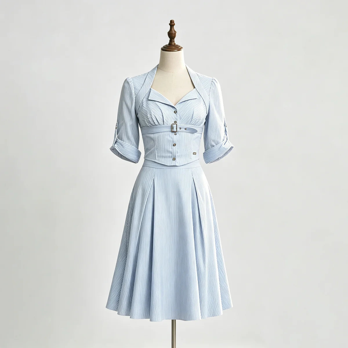 A light blue and white vertically striped vintage-style dress displayed on a mannequin. The dress features a structured, cinched waist with a decorative belt and button details, short puff sleeves, and a flared skirt.